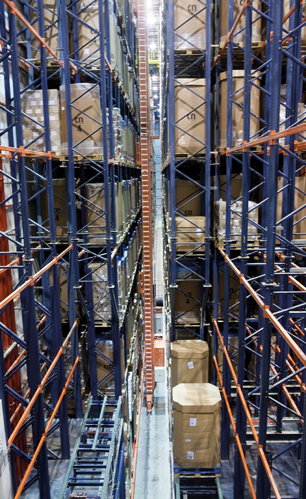 In each aisle, the twin-mast stacker cranes move pallets between input and output conveyors and rack locations