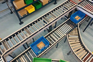 The conveyor system carries the bin to the picking station